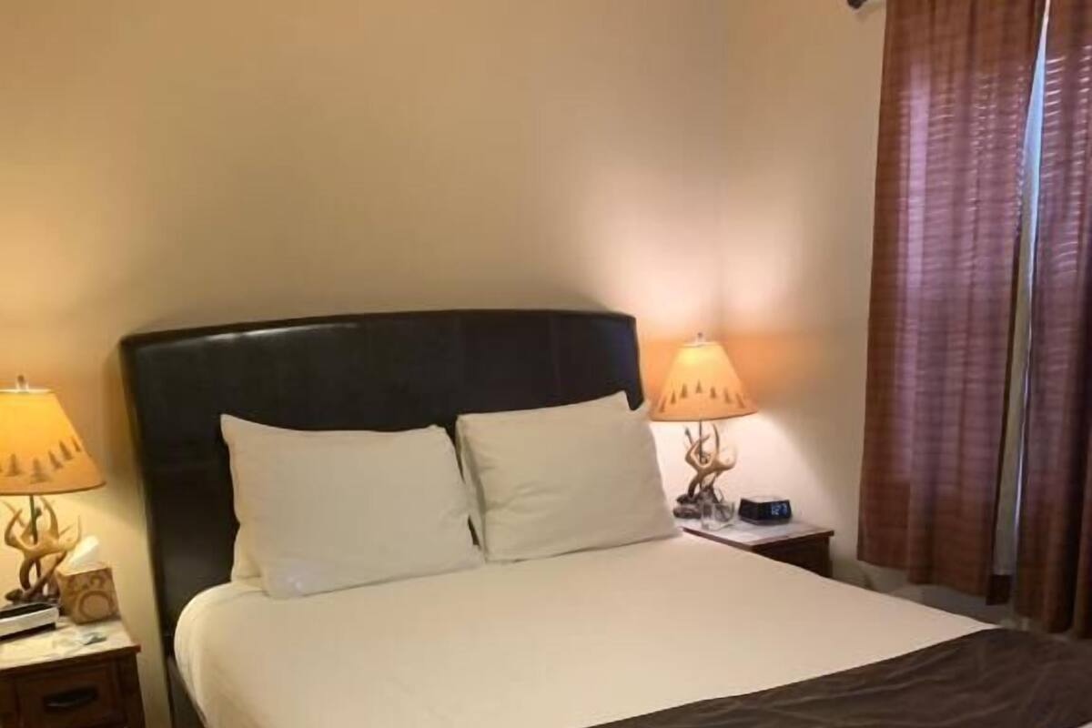 A hotel room with a large bed, two bedside tables, a lamp on each table, and a curtain on the window.
