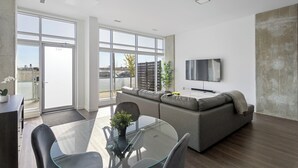 Un salon moderne avec une table à manger en verre, un canapé gris et un téléviseur à écran plat fixé au mur.