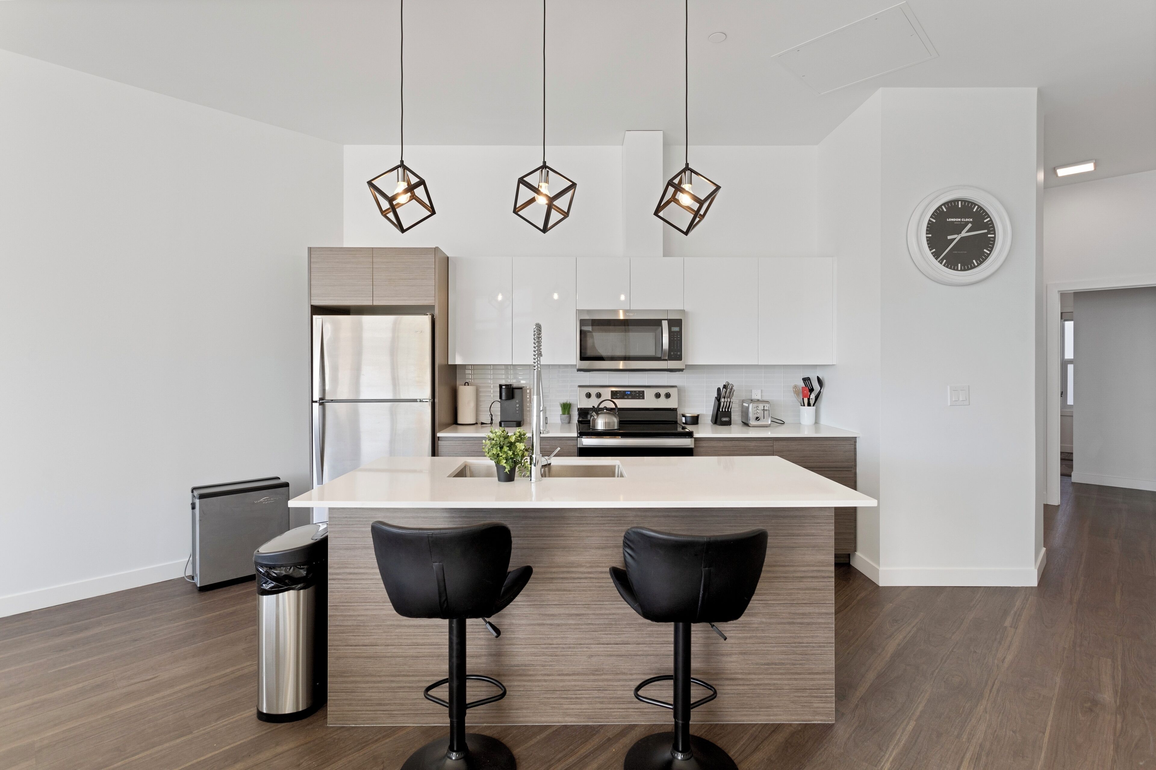 Een moderne keuken met een centraal eiland, roestvrijstalen apparatuur en zwarte barkrukken.
