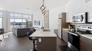 Une cuisine moderne dotée d’un îlot central, d’appareils électroménagers en acier inoxydable et de grandes fenêtres offrant une vue sur le paysage urbain.