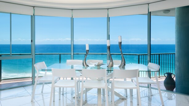 Een moderne eethoek met een glazen tafel en witte stoelen, met uitzicht op de oceaan.