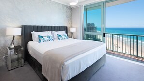 Een hotelkamer met een groot bed, twee bedlampen, een nachtkastje en uitzicht op het strand en de oceaan.
