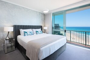 A hotel room with a large bed, two bedside lamps, a nightstand, and a view of the beach and ocean. - 2 Bedroom (1 King & 1 Bunk Bed) Ocean View apartment (Main Beach)