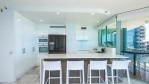 Een moderne keuken met witte kasten, een centraal eiland met barstoelen en een uitzicht op een stadsgezicht door grote ramen.