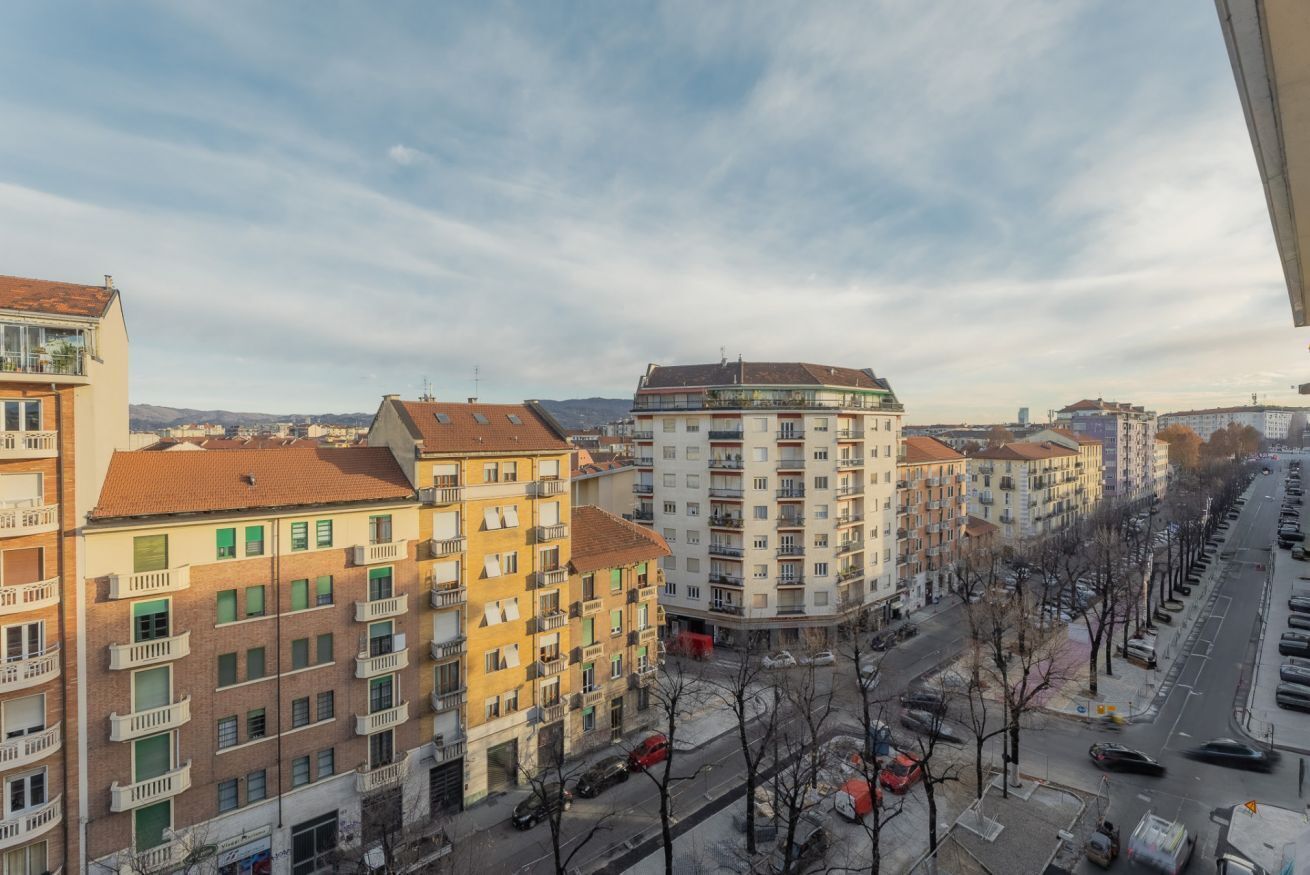 A cityscape with multi-story residential buildings, a clear sky, and a street with parked cars.