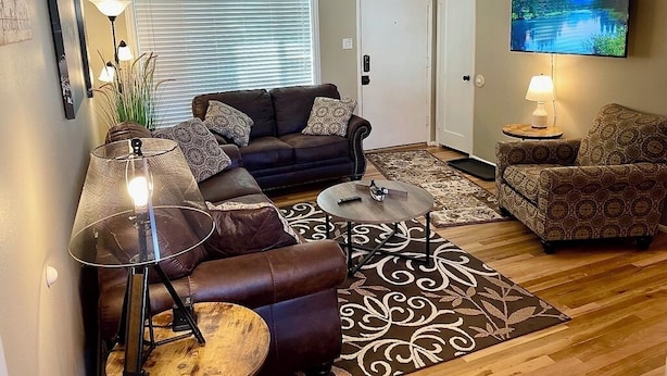 A living room with a sofa, two armchairs, a coffee table, a TV, and a lamp. - Cozy-Comfortable Linden Retreat (Idaho Falls)