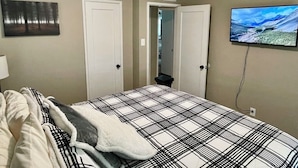 A bedroom with a bed, a television mounted on the wall, and two doors. - Cozy-Comfortable Linden Retreat (Idaho Falls)