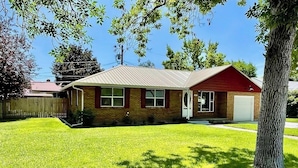 A single-story house with a red roof and a front door, surrounded by a well-maintained lawn and a wooden fence. - Cozy-Comfortable Linden Retreat (Idaho Falls)