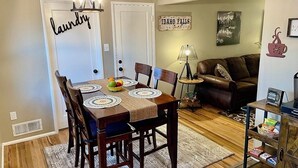A dining area with a wooden table, chairs, and placemats. There is a chandelier above the table. - Cozy-Comfortable Linden Retreat (Idaho Falls)