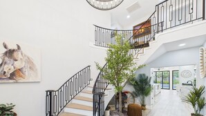 Un intérieur spacieux agrémenté d’un escalier en colimaçon, d’un grand tableau représentant un cheval et d’un espace d’accueil avec une horloge et un panneau d’accueil.