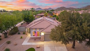 A residential property with a house featuring a tiled roof, a front yard with a small lawn, and a flag. - Desert Retreat w/ Pool, Trails & Mountain Views (Mesa)