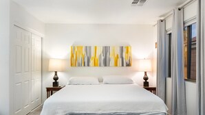 A hotel room with a bed, two bedside lamps, a large abstract painting, and a window with curtains. - Desert Retreat w/ Pool, Trails & Mountain Views (Mesa)