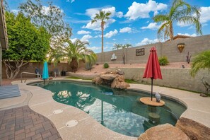 Ein Pool mit Felsen, umgeben von einer Terrasse mit Backsteinpflaster, Palmen und einer Wand mit Verzierungen.