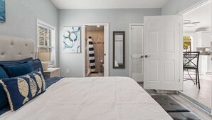 Une chambre avec un grand lit, une table de chevet, une commode, une porte et une vue sur la cuisine.