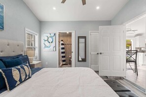 A bedroom with a large bed, a bedside table, a nightstand, a door, and a view of the kitchen. - 3BR Gulf Access • Dock + Kayaks • Gazebo • BBQ (Hernando Beach)