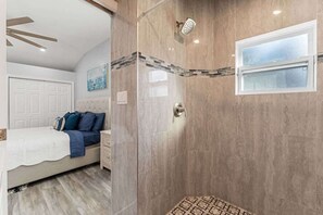 Quarto com cama, mesa de cabeceira, janela e área de chuveiro com porta de vidro.