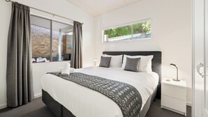 Un dormitorio ordenado con una cama grande, una mesita de noche y una ventana con cortinas.