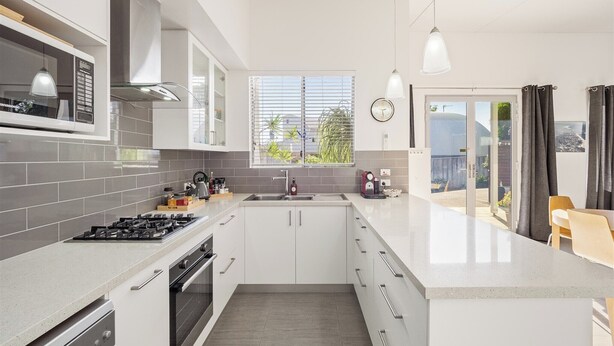 Una cocina moderna con armarios blancos, una estufa de acero inoxidable y un amplio ventanal con persianas.