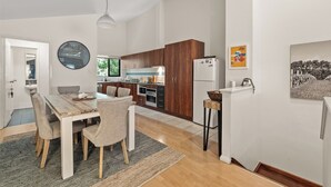 Una cucina moderna con mobili in legno, un'area pranzo con tavolo e sedie in legno, una grande sveglia a muro e un frigorifero.