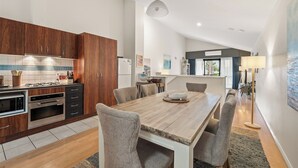Una cucina moderna con mobili in legno, una zona pranzo con tavolo e sedie in legno, e vista sul soggiorno.