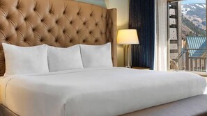 Une chambre d’hôtel avec une tête de lit capitonnée, du linge de lit blanc et une vue sur les montagnes par la fenêtre.