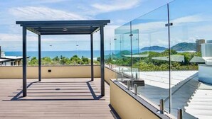 En tagterrasse med gelænder af glas, et pergola og udsigt til havet og bakkerne.