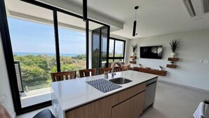 Eine moderne Küche mit einer großen Kochinsel, einer integrierten Spüle und einem großen Fenster mit Blick auf die grüne Landschaft und das Meer.