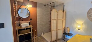 A modern bathroom with a shower, a vanity with a mirror, and a bedside table with a lamp.