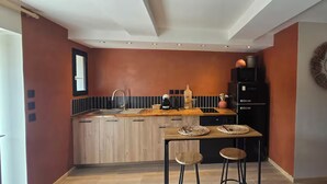 Una cocina compacta con armarios de madera, un refrigerador negro y una pequeña mesa de comedor con taburetes.