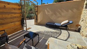 Un espacio patio con cerramiento de madera, una silla de descanso, una mesita y un muro de piedra.