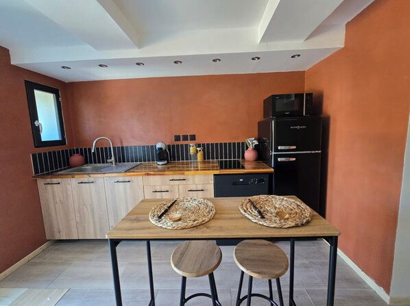 A modern kitchen with a wooden countertop, a sink, a coffee maker, and a black refrigerator.