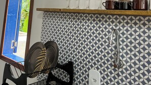 Una cucina con zoccolo decorato, uno scaffale in legno con bicchieri da vino, una sedia nera e una finestra vista verde.