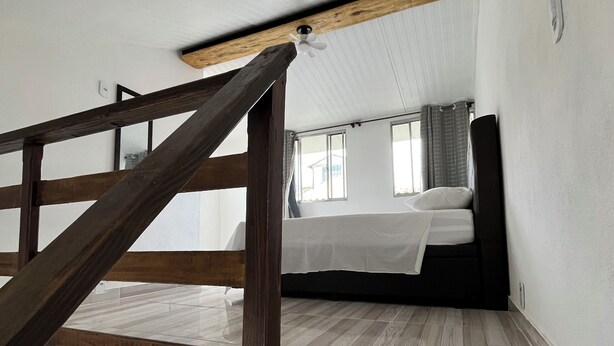 Una stanza con una scala in legno, un letto e una finestra.