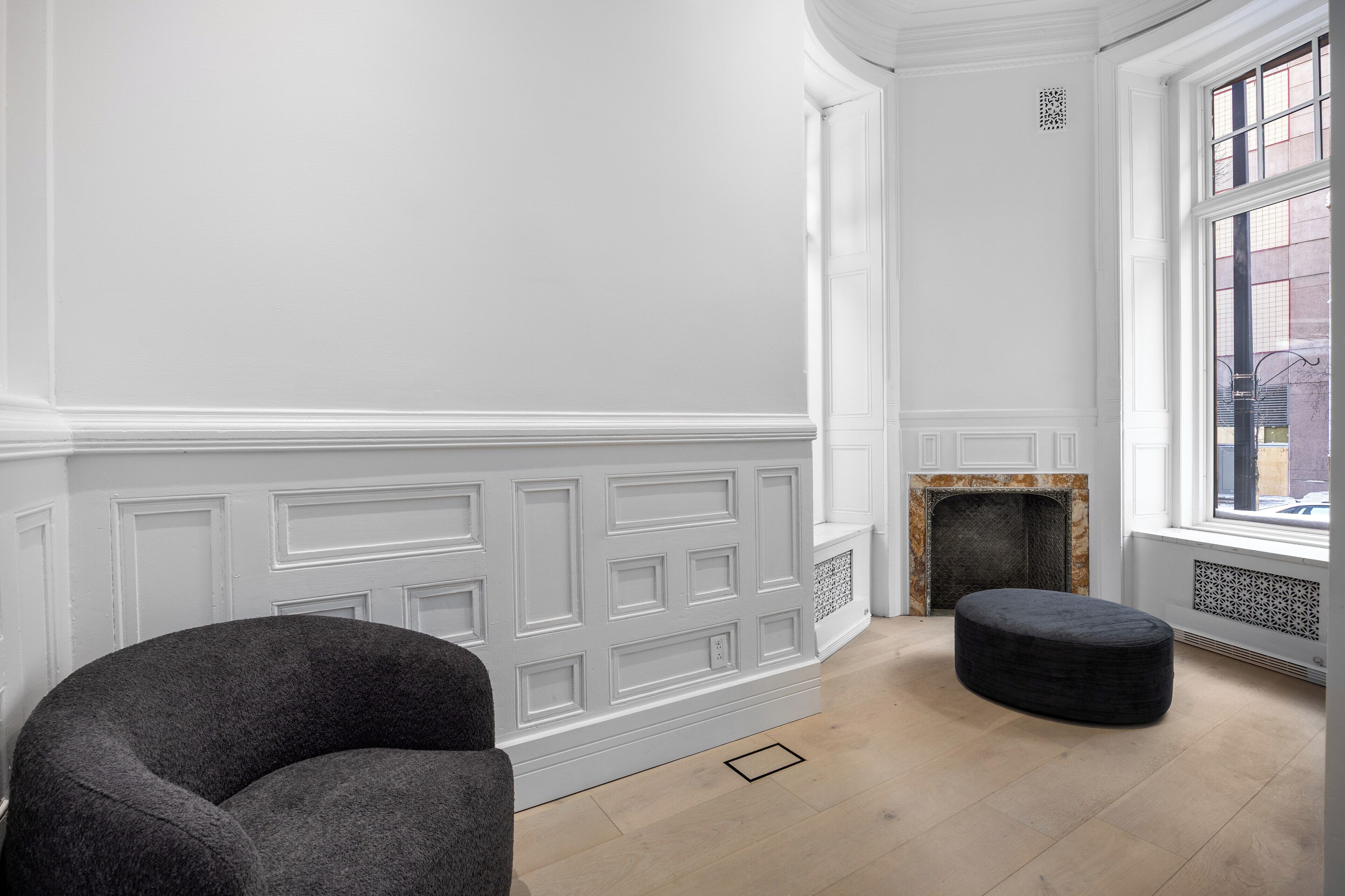 Ein Zimmer mit Kamin, großem Fenster und einem dunkelgrauen Sessel.