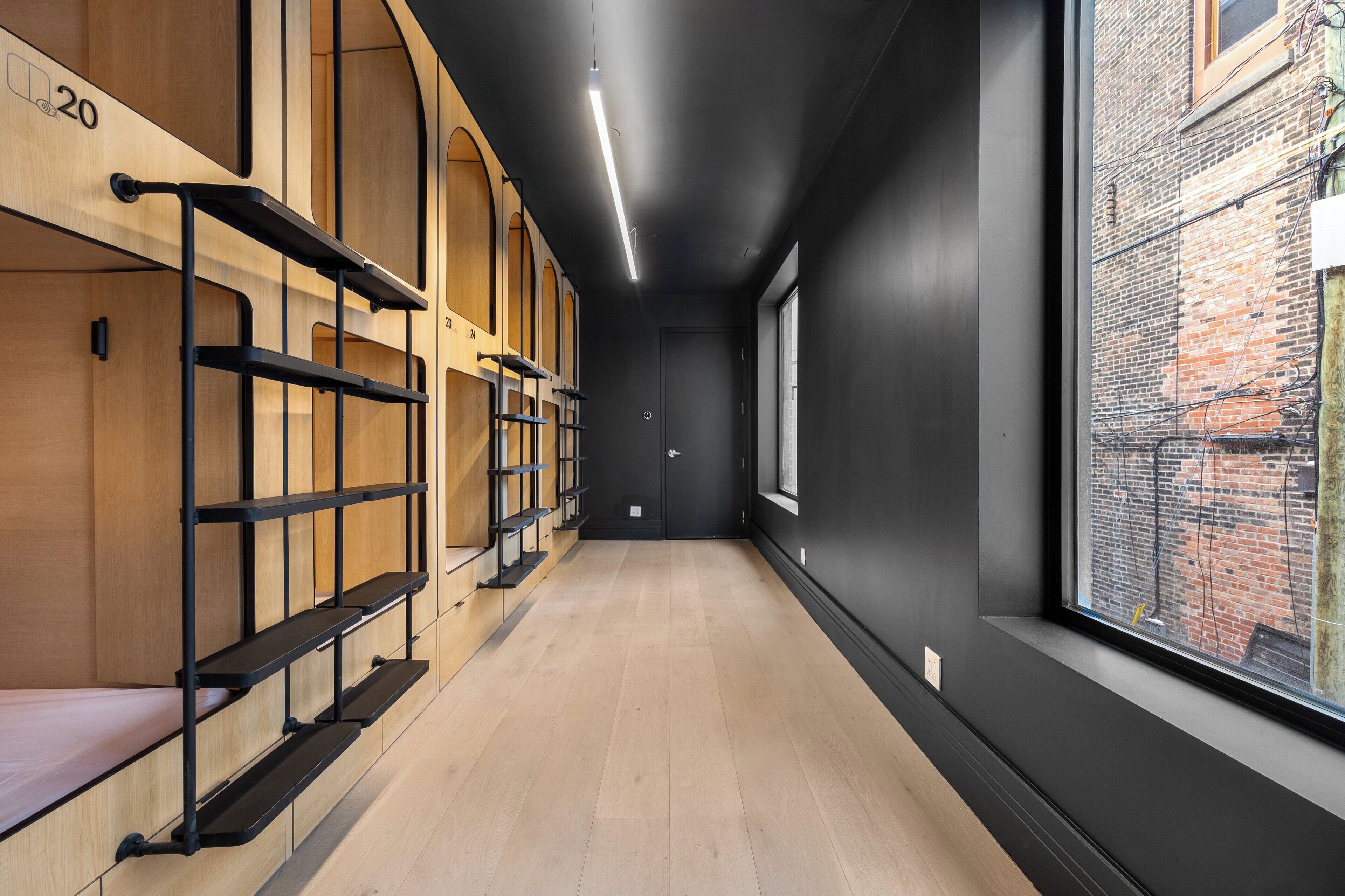 A hallway with bunk beds, a wooden floor, and a large window with a view of a brick building.