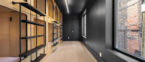 A hallway with bunk beds, a wooden floor, and a large window with a view of a brick building.