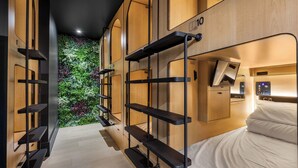 Una habitación de hotel moderna con una cama litera, estanterías empotradas, un escritorio pequeño con una computadora y una pared verde adornada con flores.