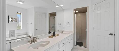 A modern bathroom with a double sink vanity, a large mirror, and a walk-in shower.