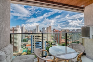 A balcony with a glass table and wicker chairs, overlooking a cityscape with high-rise buildings and a clear sky. - Beach Class Meireles by Carpediem Ocean View (Fortaleza)