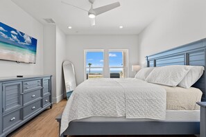 A bedroom with a bed, a dresser, a ceiling fan, and a view of the ocean.