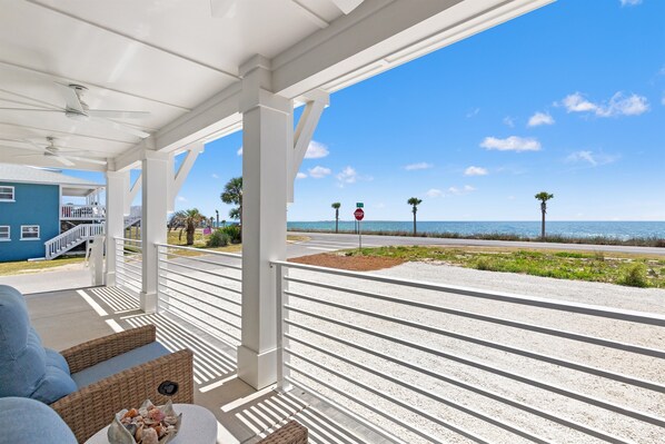 A covered porch with a view of the ocean, a stop sign, and a blue building in the background.