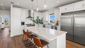 Una cocina moderna con armarios blancos, electrodomésticos de acero inoxidable, una isla de mármol e iluminación colgante.
