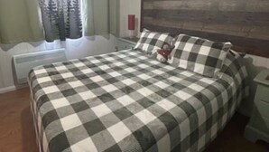 A bedroom with a checkered bedspread, a wooden headboard, a ceiling fan, and a window with curtains.