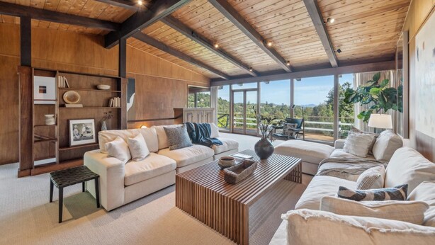 Amplio salón con techo alto, estanterías de madera empotradas y un gran ventanal con vistas panorámicas.