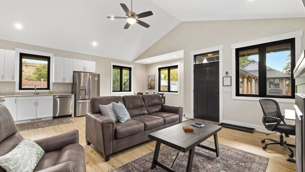 A modern living room with a brown leather sofa, a coffee table, and a ceiling fan. - Newly Built 1BR Cottage - Rock Creek Cottages #5 (Red Lodge)