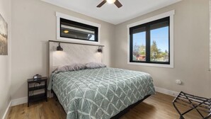 A bedroom with a bed, a nightstand, a ceiling fan, a window, and a view of the outside. - Newly Built 1BR Cottage - Rock Creek Cottages #5 (Red Lodge)