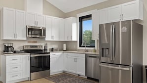 A modern kitchen with white cabinets, stainless steel appliances, and a built-in oven. - Newly Built 1BR Cottage - Rock Creek Cottages #5 (Red Lodge)