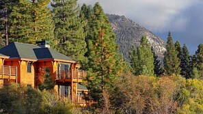 A wooden cabin with a balcony, surrounded by dense forest and a mountain backdrop. - Lake Tahoe 2BR Lodge Villa – Fireplace, Full Kitchen & Steps to Incline Village (Incline Village)