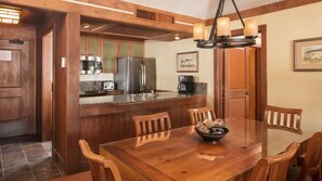Puisesta ruokapöydästä ja tuoleista koostuva ruokailutila, ruoanlaittotila, jossa on ruostumattomasta teräksestä valmistettuja kodinkoneita, sekä seinällä oleva kehystetty taulu.