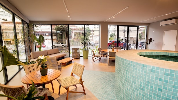 Un espace piscine intérieur moderne, avec un mur incurvé revêtu de carreaux bleus, des meubles en bois et de grandes fenêtres donnant sur la rue.